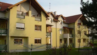 Mehrfamilienhaus mit gelber Fassade, Balkonen und einem Gemeinschaftsgarten mit Spielplatz.