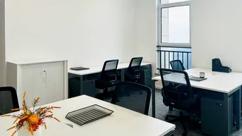 Heller Büroraum mit mehreren Arbeitsplätzen, großen Fenstern und moderner Einrichtung für produktives Arbeiten.