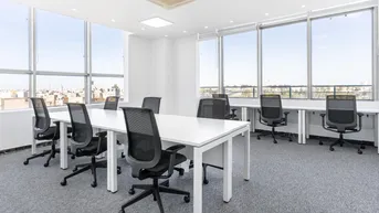 Helles, modernes Büro mit großen Fenstern, Blick auf die Stadt und mehreren Arbeitsplätzen.