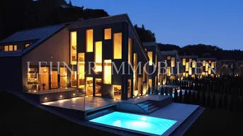 Moderne Villa bei Nacht mit beleuchtetem Pool und Terrasse, umgeben von gepflegter Landschaft.