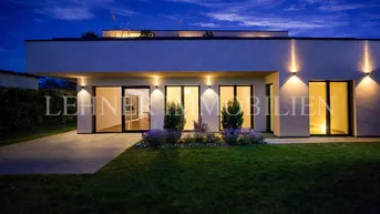 Moderne Architektur des Hauses bei Nacht, beleuchtet mit Außenstrahlern und gepflegtem Vorgarten.