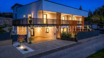 Modernes Mehrfamilienhaus bei Nacht mit beleuchteter Fassade und Einfahrt, umgeben von Bäumen.