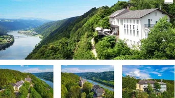 Luftaufnahme eines Hotels und weiterer Gebäude in einer malerischen Flusslandschaft umgeben von grünen Hügeln.
