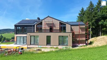 Modernes Haus im Bau mit Holzfassade, großen Fenstern und Solarpaneelen auf dem Dach.