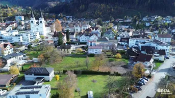 Luftaufnahme einer malerischen Stadt mit Kirche, Wohngebäuden und grünen Hügeln im Hintergrund.