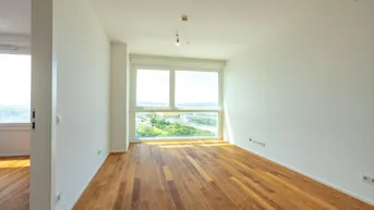 Helles Zimmer mit Holzboden und großen Fenstern, die einen weiten Blick ins Grüne bieten.