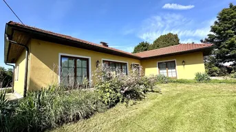 Rückansicht des gelben Hauses mit Ziegeldach, umgeben von grünem Rasen und Sträuchern.