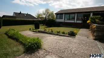 Vorderansicht des Hauses mit gepflegtem Rasen, Blumenbeeten und einem gepflasterten Weg.
