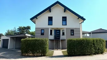 Modernes Einfamilienhaus mit gepflegter Fassade, Carport und grünen Hecken im Vorgarten.