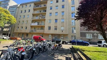 Mehrstöckiges Wohngebäude mit Balkonen und Fahrrädern im Vordergrund, umgeben von Bäumen.