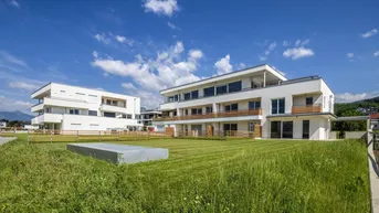 Moderne Wohngebäude mit weißer Fassade, Balkonen und gepflegter Grünfläche unter blauem Himmel.