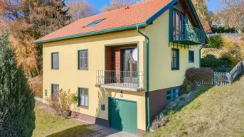 Gelbes Einfamilienhaus mit grünen Akzenten, Balkonen und Garage in ländlicher Umgebung.