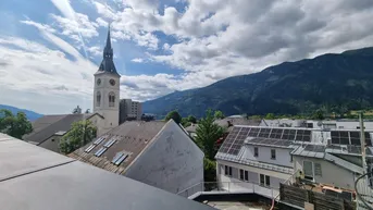 Panoramablick über die Stadt mit Kirche, umliegenden Gebäuden und majestätischen Bergen im Hintergrund.