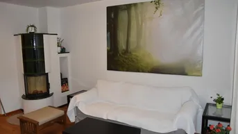 Gemütliches Wohnzimmer mit Kachelofen, bequemer Couch und einem großen Wandbild.