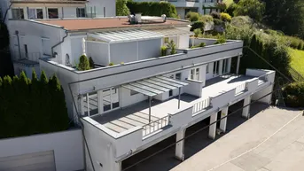 Moderne Architektur mit mehreren Terrassen und integrierter Garage, umgeben von grüner Landschaft.
