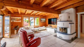 Helles Wohnzimmer mit Holzwänden, Fliesenboden und einem traditionellen Kachelofen.