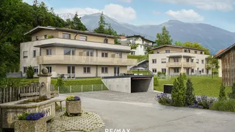 Moderne Wohnanlage mit mehreren Gebäuden, Tiefgaragenzufahrt und beeindruckendem Bergblick im Hintergrund.