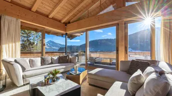 Helles Wohnzimmer mit großen Glasfronten, Holzbalkendecke und atemberaubendem Bergblick.