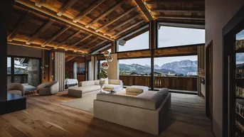 Geräumiges Wohnzimmer mit Holzbalkendecke, großen Fenstern und atemberaubendem Bergblick.