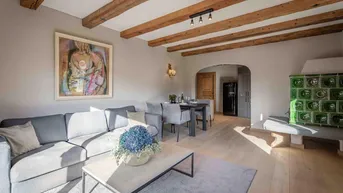 Gemütlicher Wohn-Essbereich mit Holzbalkendecke, modernem Sofa und traditionellem Kachelofen.