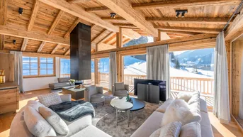 Helles Wohnzimmer im Chalet-Stil mit Holzbalken, Kamin und Panoramablick auf die verschneite Berglandschaft.