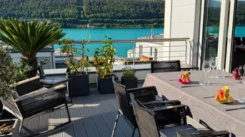 Geräumige Terrasse mit Esstisch, Pflanzen und herrlichem Blick auf den See und die Berge.