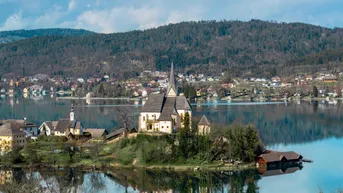 Malerischer Blick auf den Wörthersee mit der Wallfahrtskirche Maria Wörth und umliegenden Häusern.