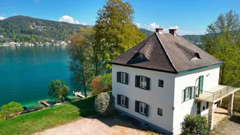 Idyllisches Haus am Seeufer mit Bergblick und kleinem Balkon, umgeben von grüner Natur.