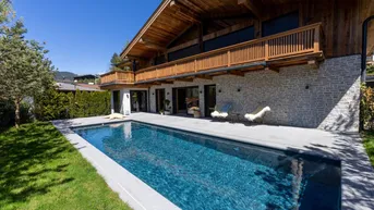 Modernes Chalet mit Außenpool, Steinfassade und Holzdetails unter blauem Himmel.