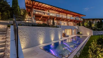 Luxuriöses Anwesen bei Nacht mit beleuchtetem Pool und moderner Holzarchitektur.