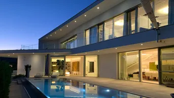 Moderne Villa bei Dämmerung mit beleuchtetem Pool und großen Glasfronten, die den Innenbereich offenbaren.