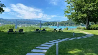 Gepflegte Rasenfläche mit Steinweg, Liegestühlen und weitem Blick auf den See und die Berge.