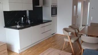 Moderne offene Küche mit weißen Schränken, dunkler Arbeitsplatte und angrenzendem Essbereich.