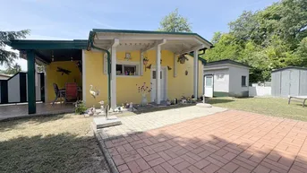 Gelbes Haus mit überdachtem Eingangsbereich, gepflastertem Vorplatz und Rasenfläche unter blauem Himmel.