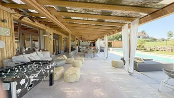 Große überdachte Terrasse mit Lounge-Möbeln, Esstisch und Tischfußball, ideal für Unterhaltung im Freien.