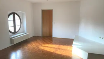 Helles Zimmer mit Fischgrätparkett, runden Fenstern und weiß gestrichenen Wänden.