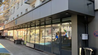 Moderne Geschäftsfassade mit großen Glasfenstern und einem Vordach, das den Eingangsbereich schützt.