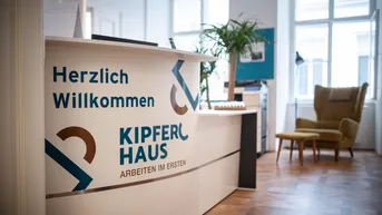 Empfangsbereich mit Willkommensschild, Parkettboden und gemütlichem Sessel am Fenster.
