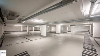 Geräumige und gut beleuchtete Tiefgarage mit vielen Stellplätzen und moderner Lüftungsanlage.