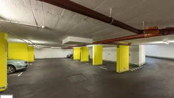 Geräumige Tiefgarage mit markierten Stellplätzen und gelben Säulen für Bewohner.