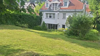 Großzügiger Gartenbereich mit Rasenfläche und Blick auf die weiße Villa mit rotem Ziegeldach.