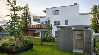 Modernes weißes Mehrfamilienhaus mit Balkonen, gepflegtem Rasen und einem Hochbeet im Vorgarten.