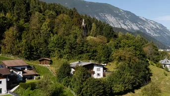 Idyllisches Haus in Hanglage, umgeben von Wald und Bergen unter blauem Himmel.