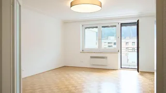 Helles Zimmer mit Parkettboden, großem Fenster und Zugang zu einem Balkon oder einer Terrasse.