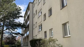 Mehrfamilienhaus mit heller Fassade und gepflegter Grünanlage unter blauem Himmel.
