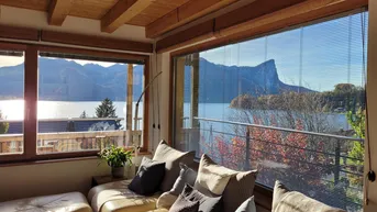 Helles Wohnzimmer mit Panoramablick auf den See und die umliegende Berglandschaft durch große Fenster.