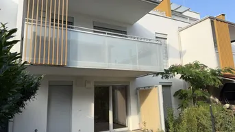 Moderne Wohnanlage mit Balkon und einer gepflasterten Terrasse im Erdgeschoss, umgeben von Grünflächen.