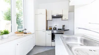 Kompakte Einbauküche mit weißen Schränken, Spüle und Fenster mit Blick ins Grüne.