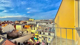 Balkon mit Blick über die Stadt und die umliegenden Dächer unter einem weiten blauen Himmel.