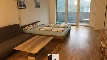 Helles Wohnzimmer mit Holzboden, Schlafbereich und Zugang zu einem Balkon mit Bergblick.